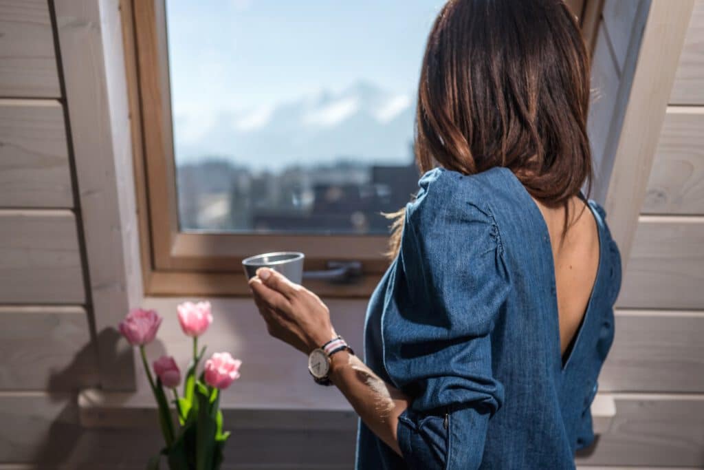A guest with a cup beside a window overlooking the mountains